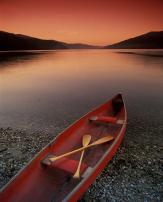 Red afterglow of a sunset over a mountain lake with canoe resting on the shoreline.